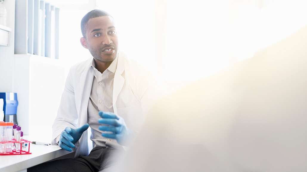 A male scientist sitting at a workspace with test tubes.