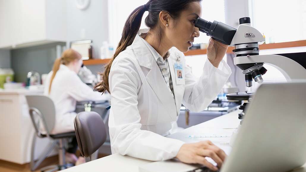 Two female scientists in their lab, both looking into microscopes.