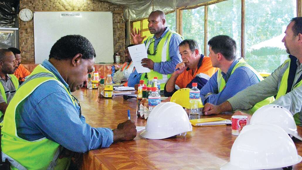 Workers in neon vests gathered around a table for a meeting