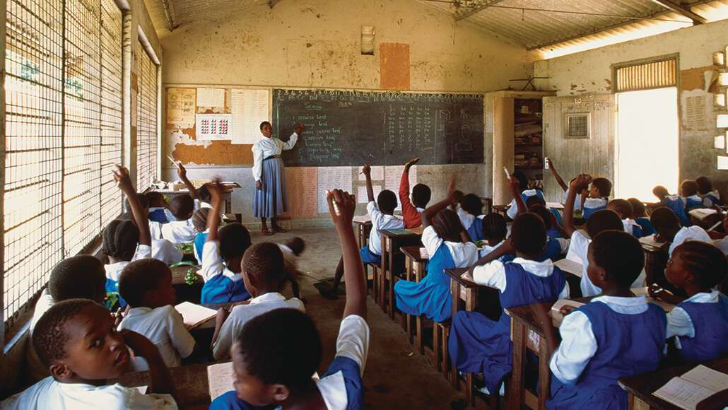 Teacher in classroom pointing to blackboard, Kenya