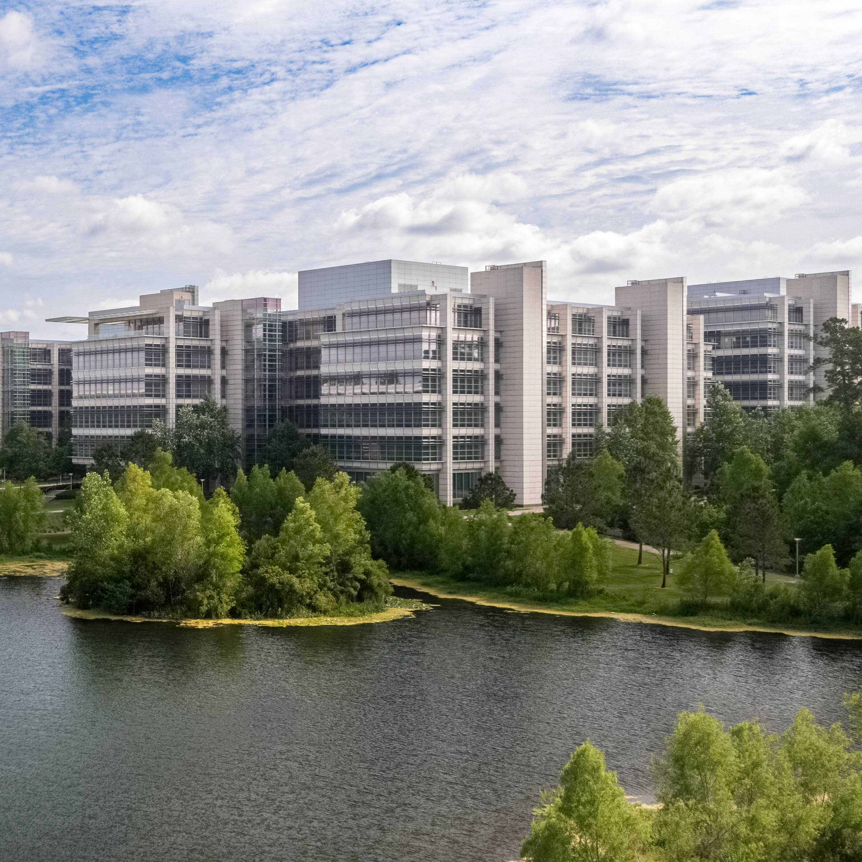 Office buildings sitting at the edge of a lake with blue skies in the background.