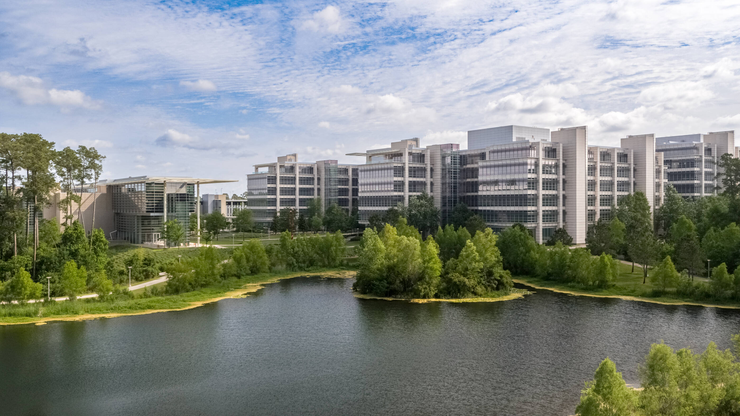 Office buildings sitting at the edge of a lake with blue skies in the background.