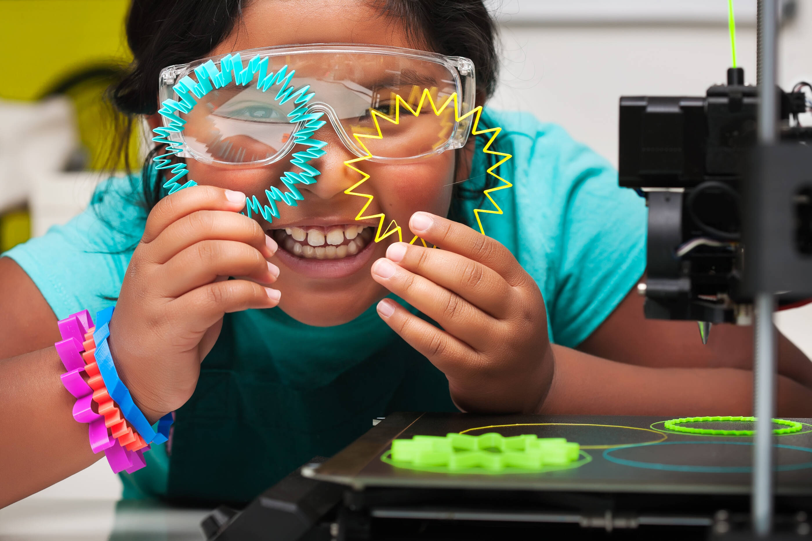 Happy STEM student smiles and shows off the colorful 3d printed shapes, plastic parts on the print bed with skirt for plate adhesion.