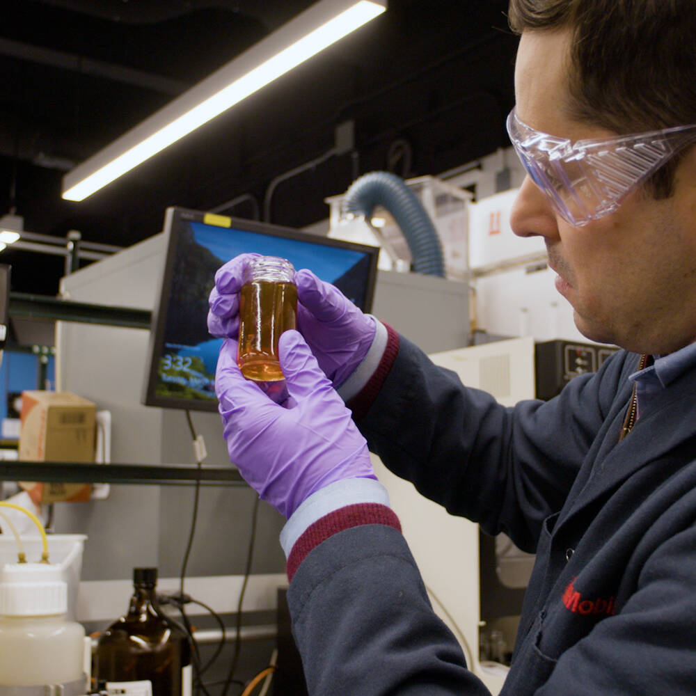 Man in lab wearing safety goggles and holding a glass jar of liquid